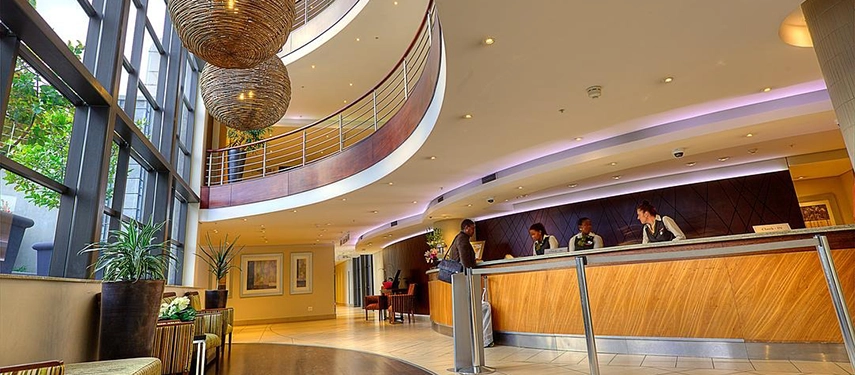 A bright, multi-level reception area featuring sweeping curved balconies, oversized woven pendant lights, and a welcoming wood-panelled front desk.
