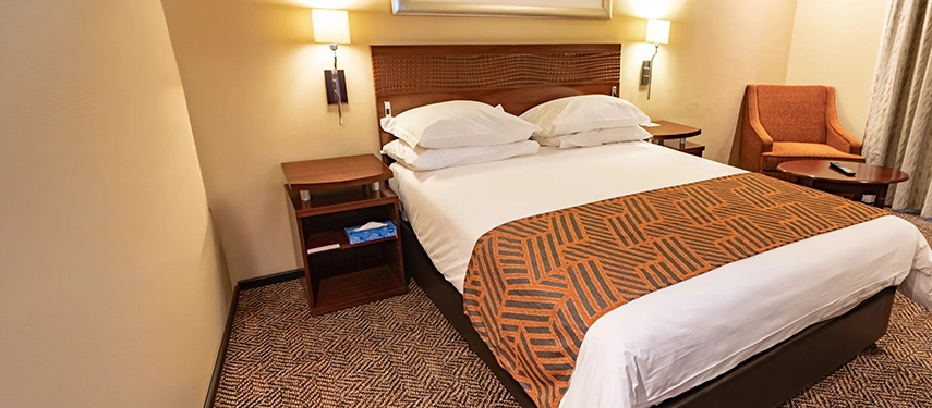 A cosy, well-appointed sanctuary featuring crisp white linens, warm ambient lighting, and a distinctive geometric bed runner to ensure a restful haven between travels.