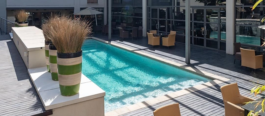 A sparkling outdoor swimming pool enhanced by a cascading stone water feature, vibrant green planters, and inviting sun loungers.