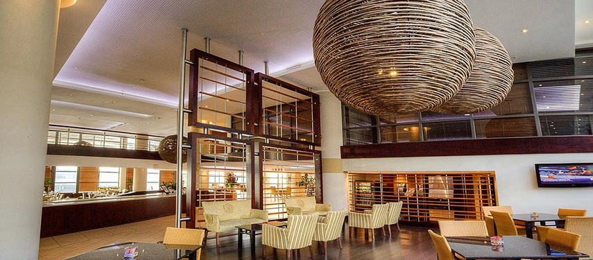 A relaxed lobby lounge area complete with comfortable patterned armchairs, warm wood accents, and oversized statement pendant lights suspended from the high ceiling.
