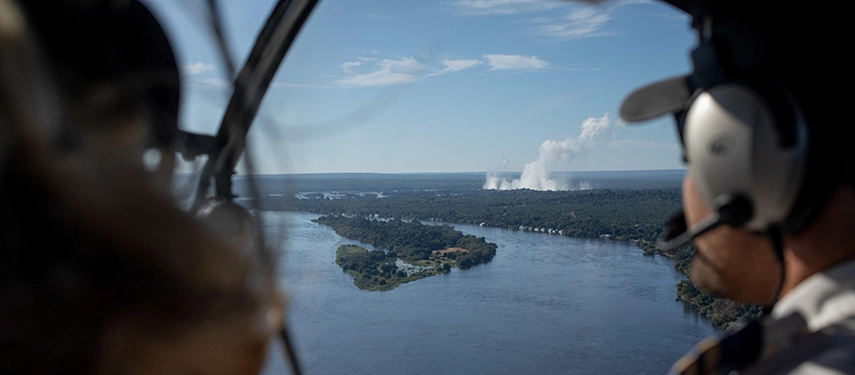 Guests enjoy a scenic helicopter flight over the Zambezi River, with sweeping views of river channels, forested islands, and the distant spray of Victoria Falls.