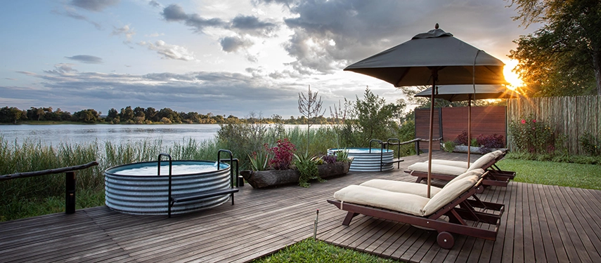 A private deck at Mukwa River Lodge overlooks the Zambezi River, with sun loungers and a circular plunge pool positioned to capture the light at sunset.
