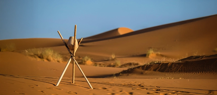 Wooden tripod and drum standing alone in the vast rolling dunes of the Sahara desert.