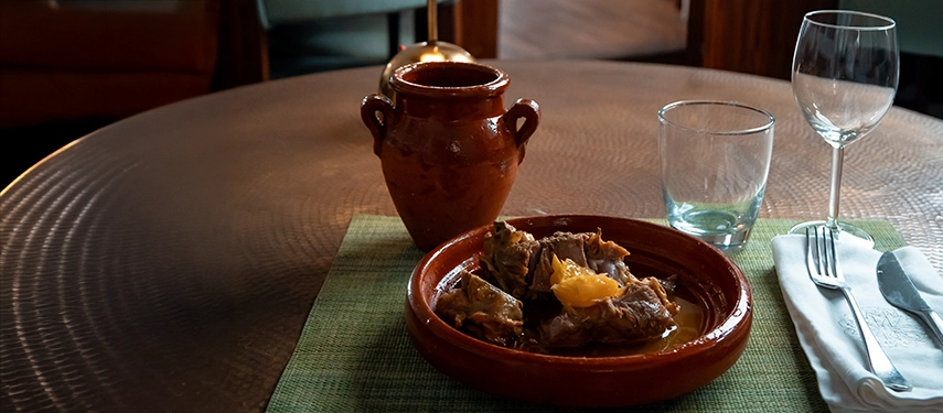 Traditional Moroccan dish served in a terracotta tagine on a dining table with glassware.